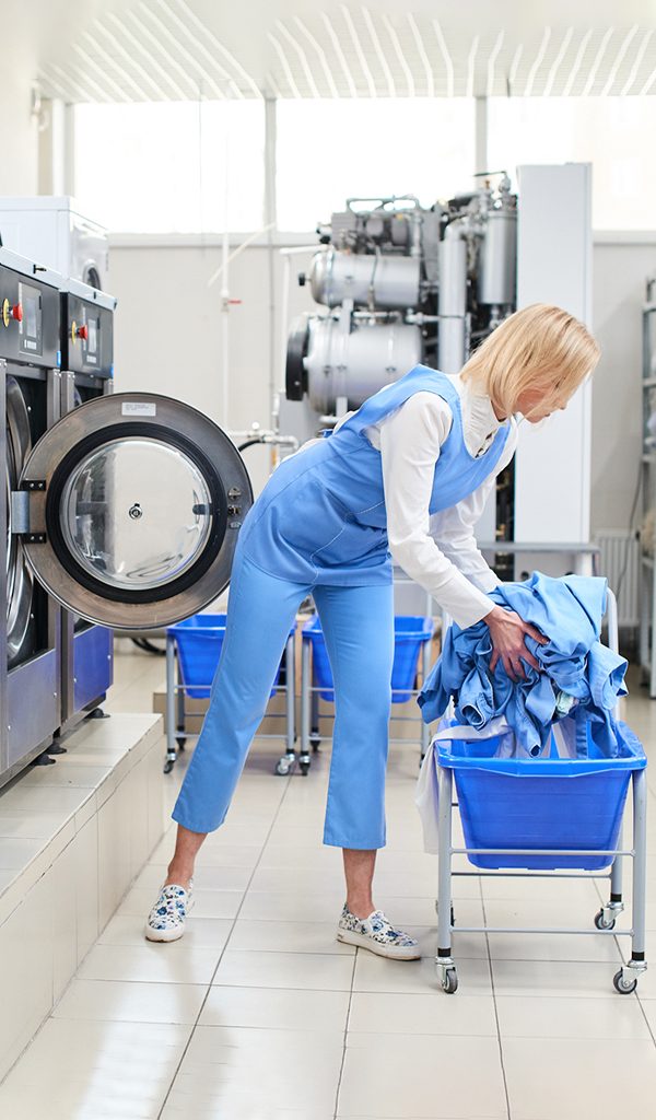 Female worker loads the Laundry clothing into the washing machine at the dry cleaners